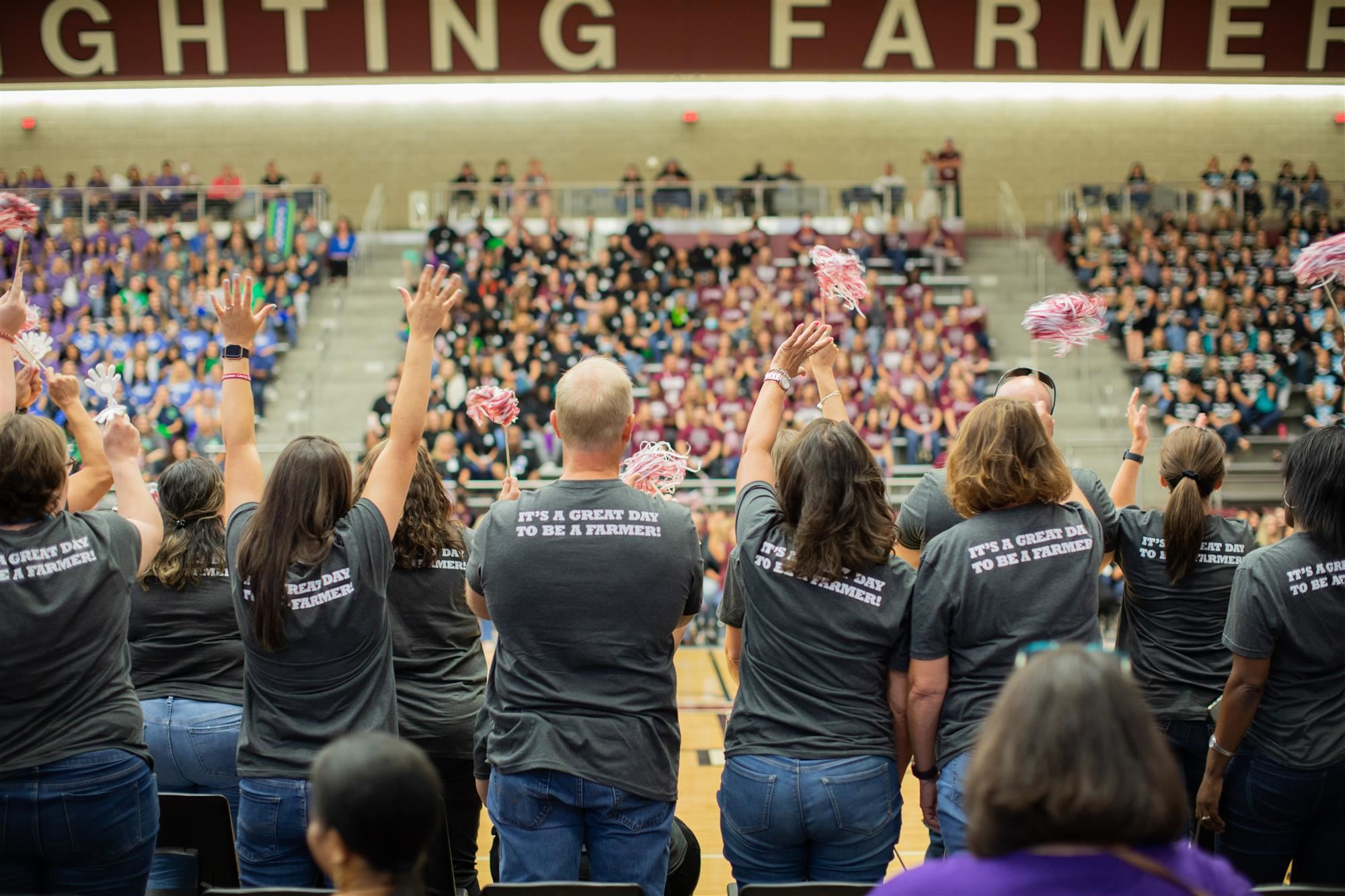 LISD staff members, wearing shirts that read "it's a great day to be a farmer," cheer next to a basketball court